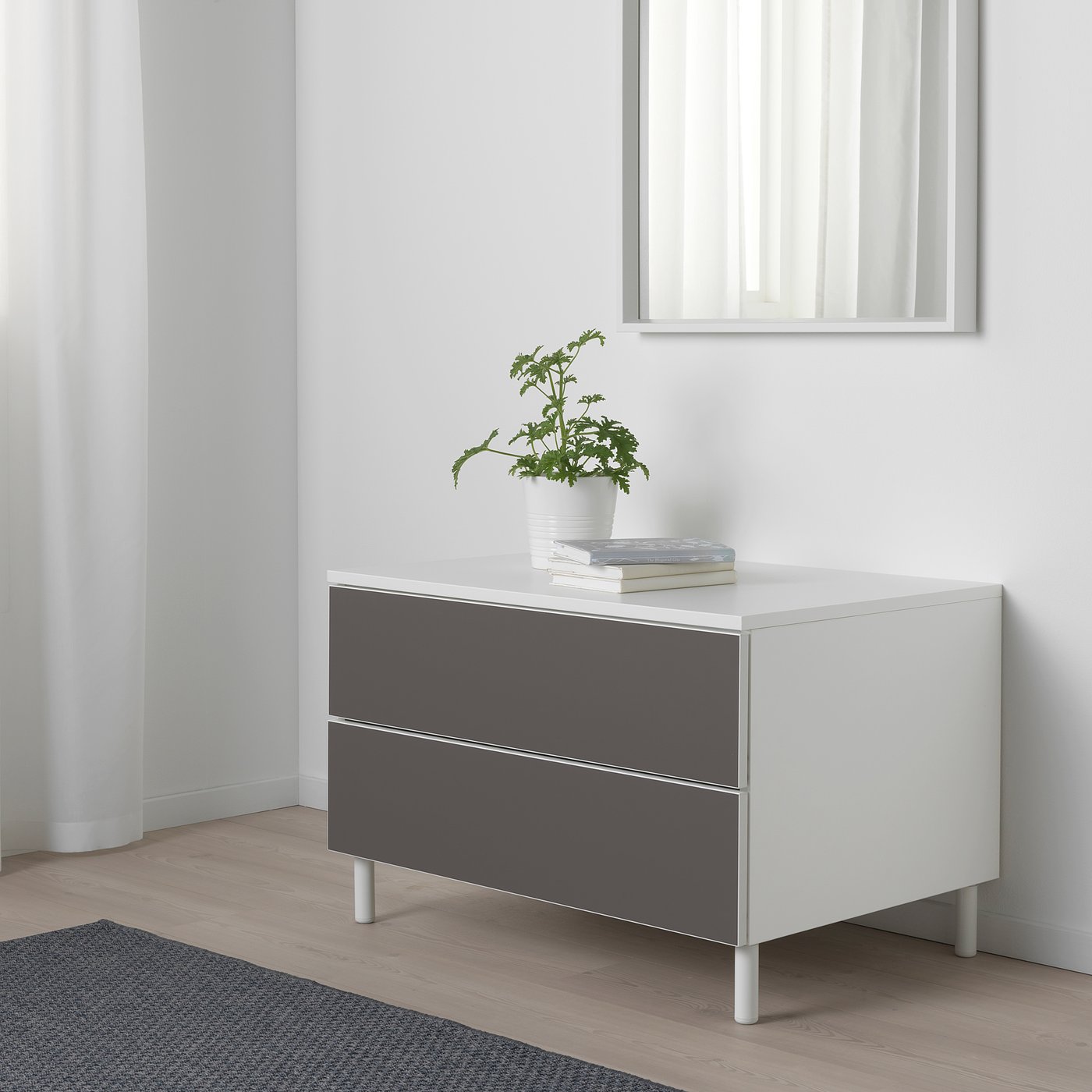 Modern PLATSA storage with 2 grey drawers, white top, plant, books, against white wall.