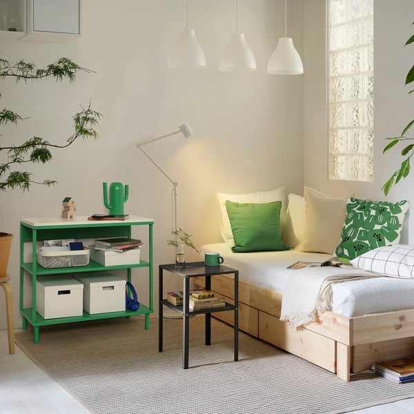 Cosy bedroom with green PLATSA shelf, books, cactus, and leafy decor.