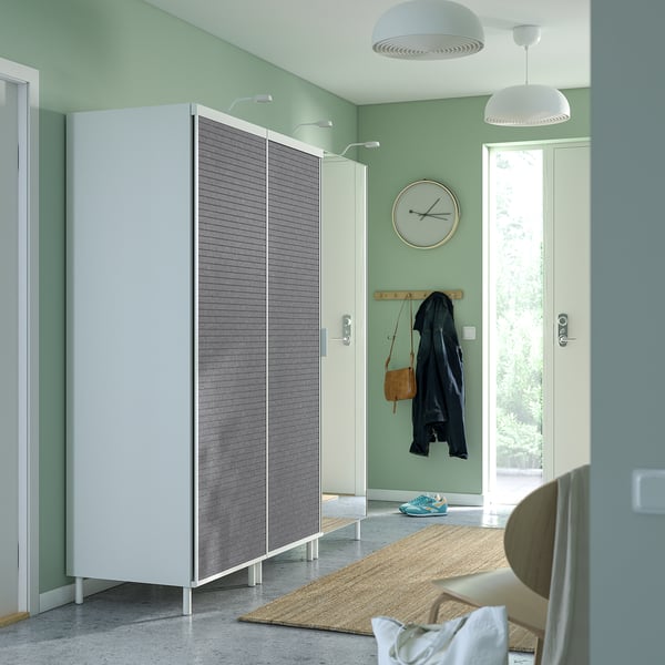 Modern entryway with white wardrobe, grey doors, hanging jackets, and a clock.