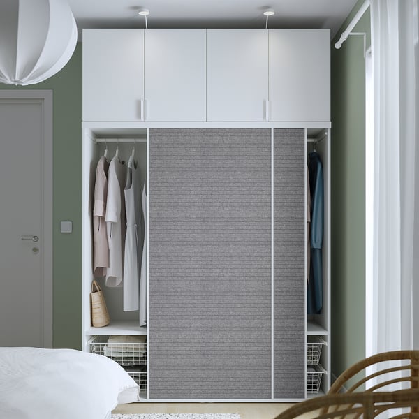 Bedroom featuring a white PLATSA wardrobe with sliding doors showcasing clothes and shelves organized with hangers and baskets.