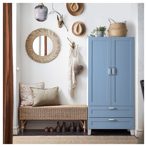 Blue PLATSA wardrobe with 2 doors & drawer, beside wicker bench with cushions. Woven hat & mirror decorate wall.