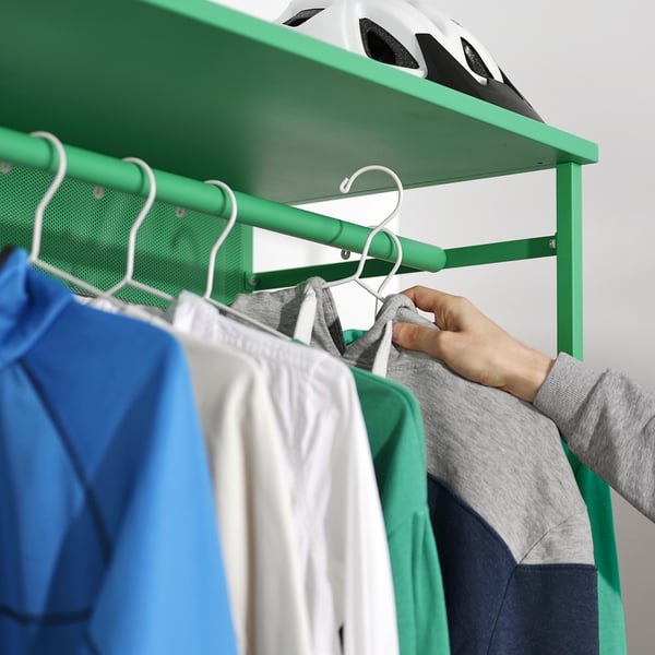 A person hangs a grey sweater on a green PLATSA clothes rack.