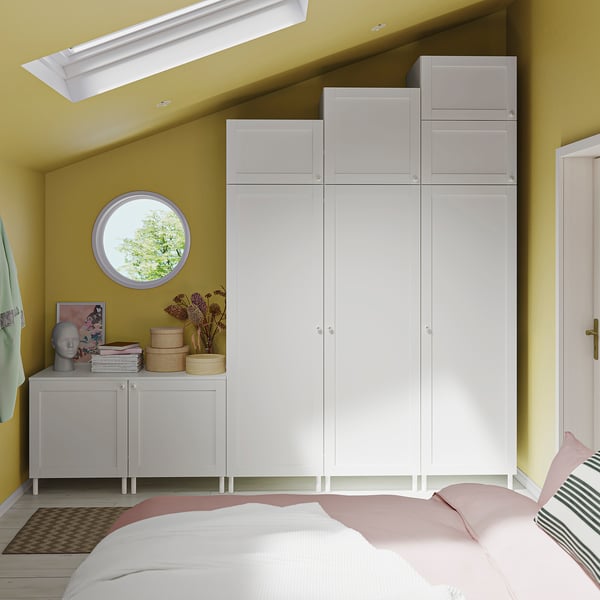 Modern bedroom with white PLATSA wardrobe, side cabinet, and bed in yellow room.