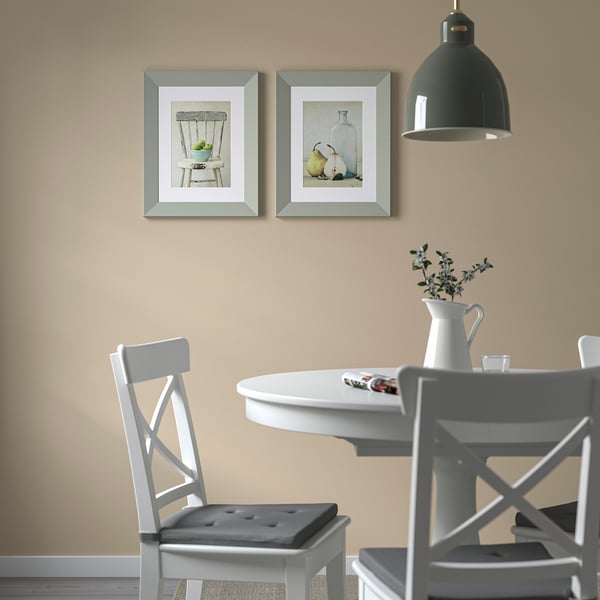 Two framed pictures over dining table with white chairs, flowers, and pendant light.