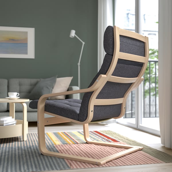 Comfortable wood armchair with dark cushions and curved back support, placed near a colourful rug in a living room with a window.