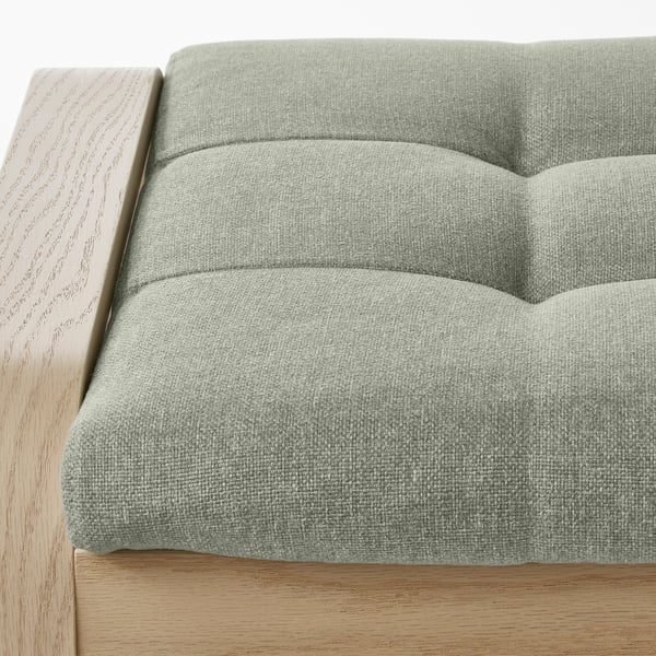 Light wood-framed footstool, upholstered in soft green fabric with plush cushions, offered for comfort.