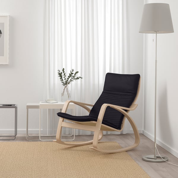 Modern living room with black POÄNG rocking chair, wooden frame, plush cushions, light beige rug, side table, floor lamp, and vase.