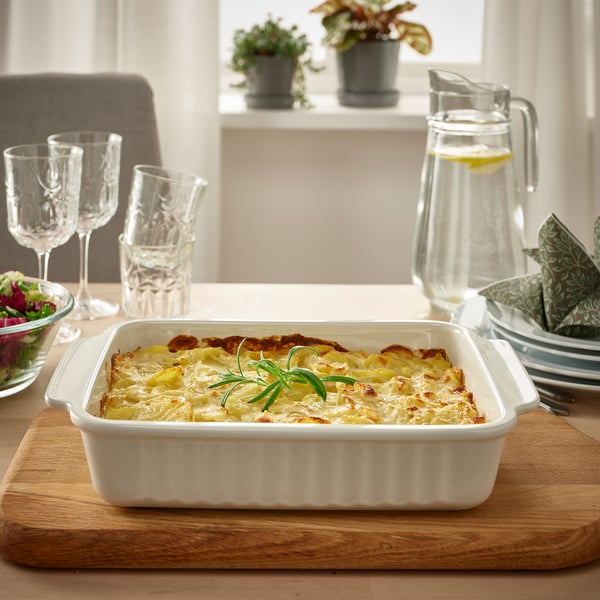 Dish of gratin on table, served in large white baking dish with handles, accompanied by glasses and pitcher.
