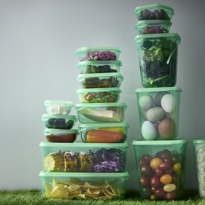 Clear, green plastic food containers, stacked with vegetables and fruits, showcasing organised fridge storage.