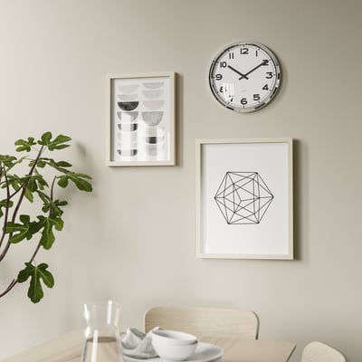 A round, white clock named PUGG with black numbers and hands, a silent quartz movement, and a stainless steel frame.