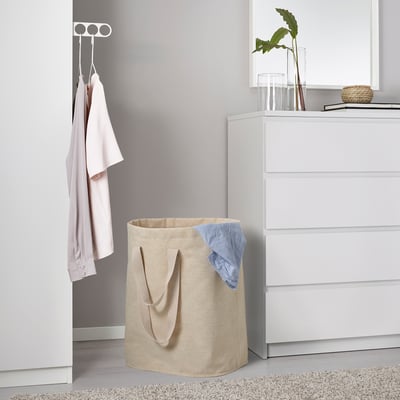 Beige laundry bag with handles near dresser, holding blue garment on rug.