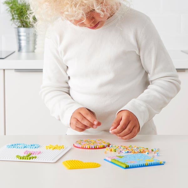 Child playing with fuse beads, creating colourful patterns on templates.