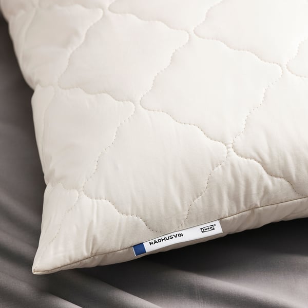 Close-up of a white, quilted pillow with RÅDHUSVIN tag, showcasing its high-quality craftsmanship and natural materials.