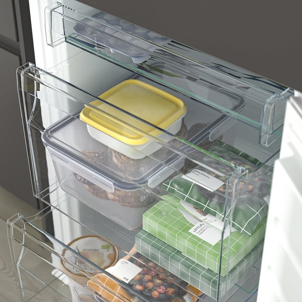 A modern fridge with clear adjustable glass shelves displaying various food items like a yellow container, nuts, and green packaged produce.
