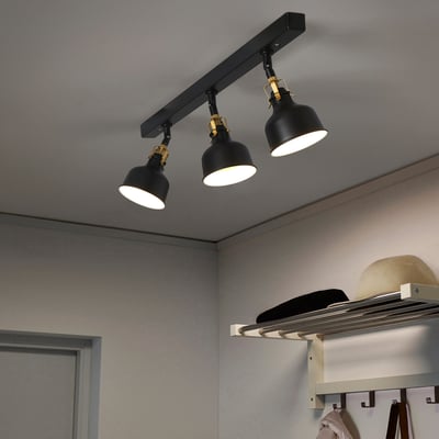A RANARP black ceiling track light with three adjustable black spotlights, attached to a wall with coats.