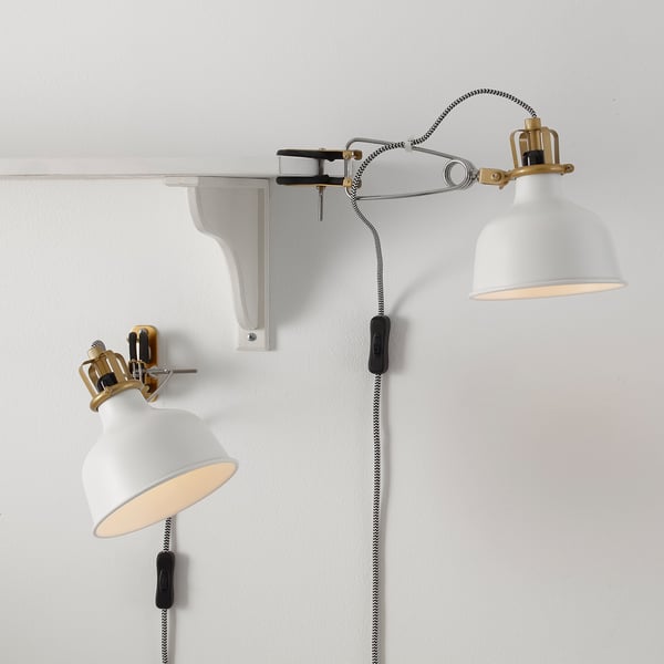 Two white RANARP lamps on a wall, one adjusted, both with cloth cords and adjustable joints.