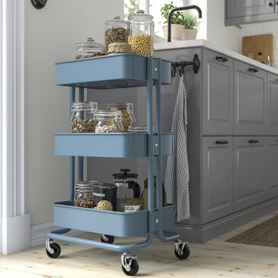 A blue ikea RÅSKOG storage trolley with three tiers and wheels for mobility. Its sturdy with a metallic finish.