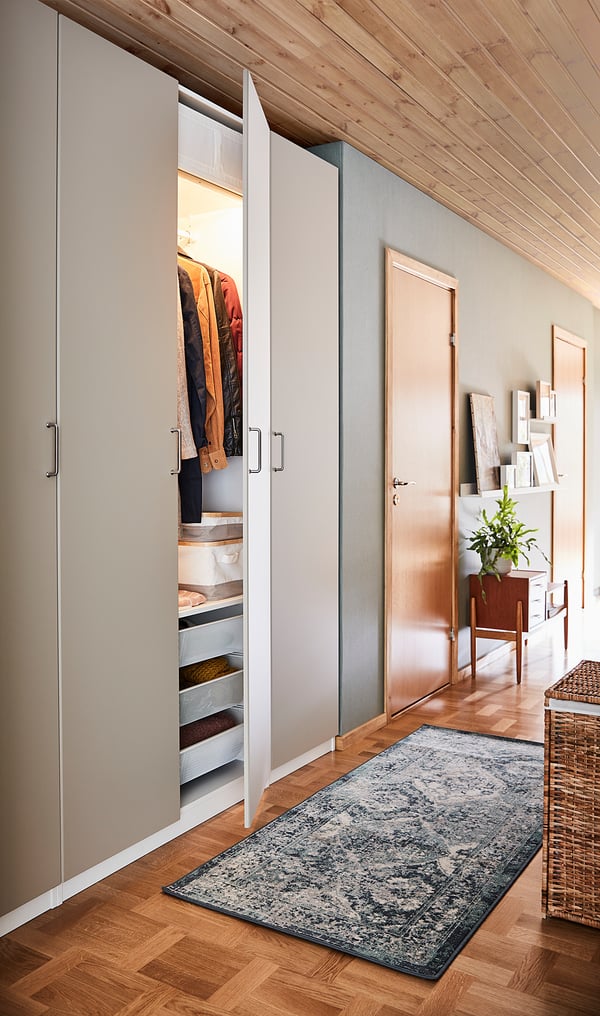 A modern closet with a beigeREINSVOLL door open, displaying clothes and shelves. Floor has a patterned rug.