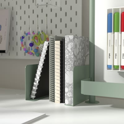 Description: green RELATERA book-ends hold notebooks. Pegboard with scissors and markers behind.