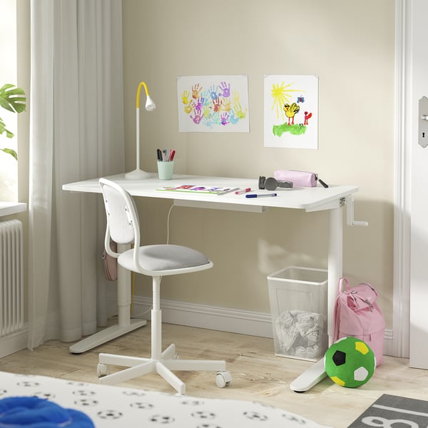 A childs study space with a white adjustable desk, chair, and wall art.