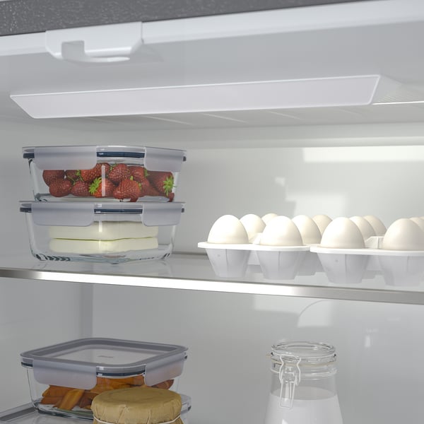Fridge with organised compartments. Top has strawberries, cheese. Bottom has various foods, including a jar.