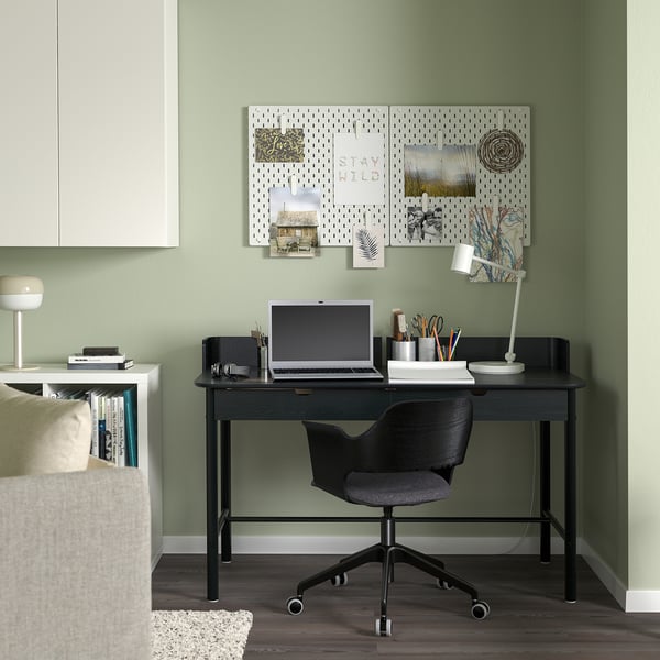A cosy green home office with a black RIDSPÖ desk and chair, featuring integrated storage and a laptop. A pegboard with notes enhances the workspace.