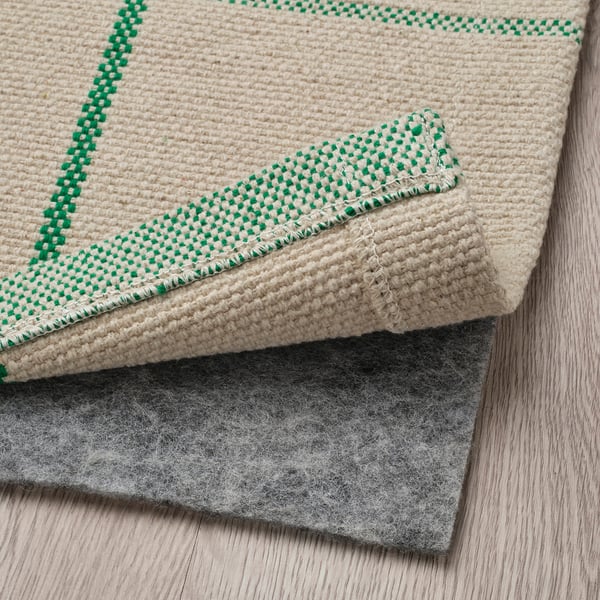 A cream rug with green checks laid on a grey felt underside, ideal for dining areas.