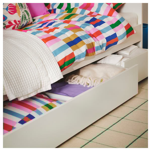 Bright striped bedding on white bed, with open drawer showing folded clothes, on beige and green rug.