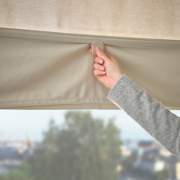 Person raising beige RINGBLOMMA roman blind with magnets, revealing outdoors.