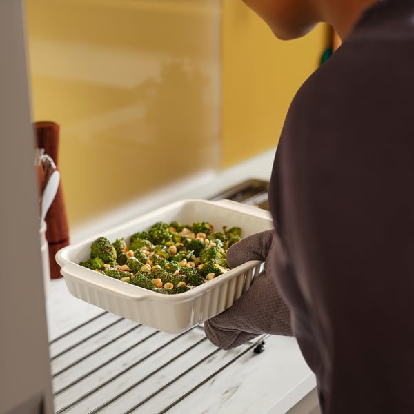 Person in oven mitts holding a dish of cooked broccoli.