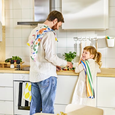 Man and child cook together, wearing colorful aprons in bright kitchen.
