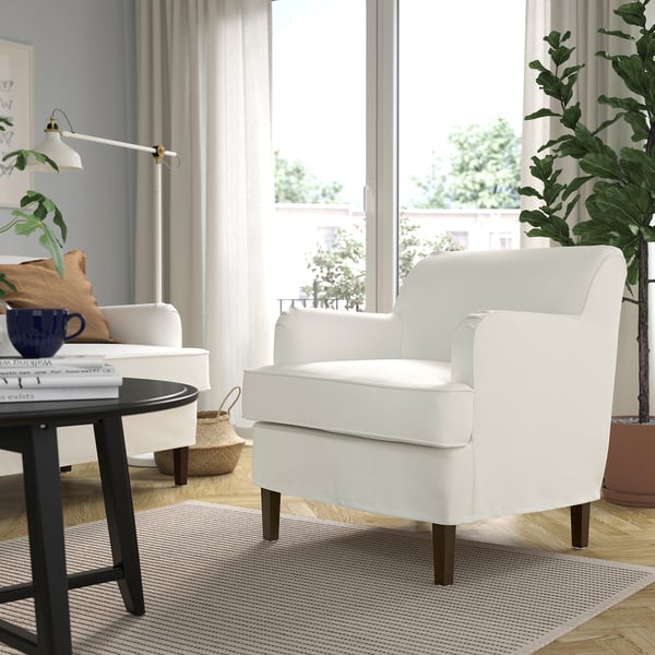 Bright living room with white ROCKSJÖN armchair, natural light, plants, cosy settings.