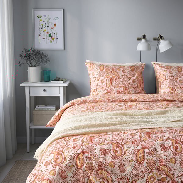 Peach paisley duvet on bed, 2 pillows, grey wall, bedside table, lamp.