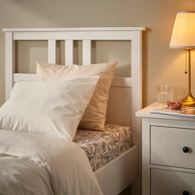 Neatly arranged bed with RODGERSIA paisley fitted sheet, white headboard, and bedside table items.