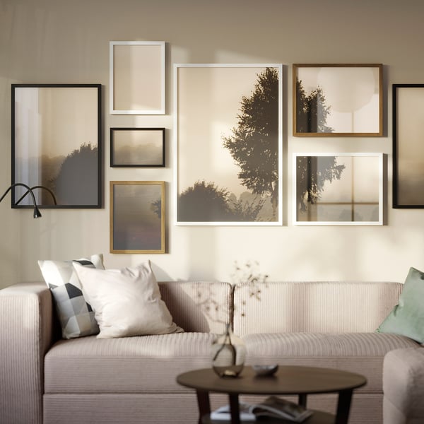 Living room with RÖDALM gallery above white couch, featuring varied art. Side table with vase completes modern design.