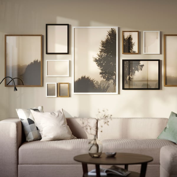 Living room with RÖDALM gallery wall above beige sofa, nature art in muted colors, coffee table with vase.