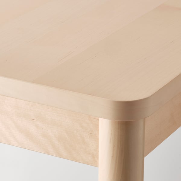 Close-up of a modern, light wood table with rounded edges and sturdy legs, showcasing smooth and durable surface.