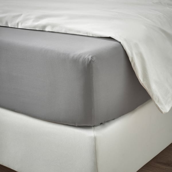 A neatly made bed with grey RÖNNVECKMAL sheets, featuring crisp percale weave, fitted over thick mattress with elastic edges.
