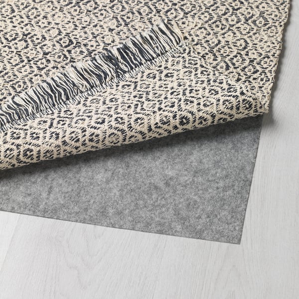 A grey leopard-print rug is shown rolled up on a light wooden floor, revealing its dark grey backside.