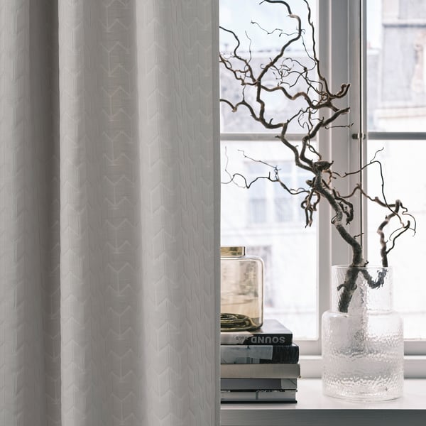 White RYSSBRÄKEN curtain with subtle pattern, covering window beside books and branching decor.