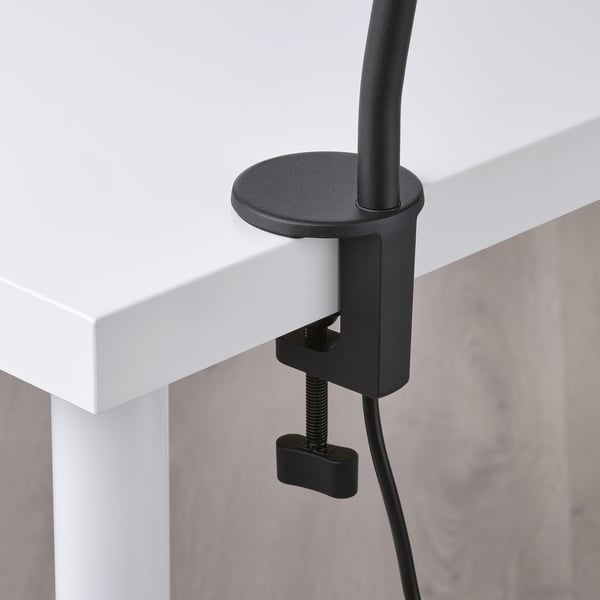 Modern lamp clamped to desk edge, adjustable neck and black clamp, quality design.