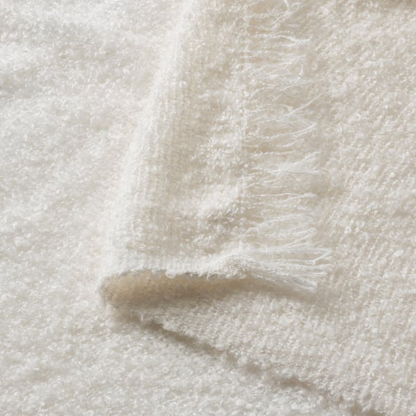 Close-up of soft, textured, off-white blanket showing crinkle-knit and fringe details.