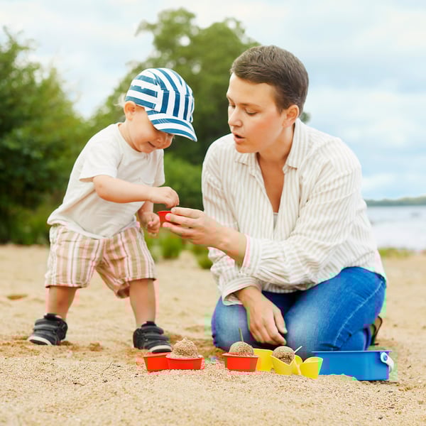 Adult and child play with sand moulds on beach.