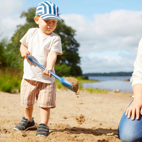 Child playing with blue sand toy on beach, pouring sand.