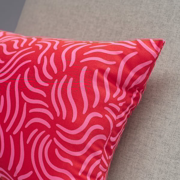 Bright red cushion with pink abstract lines rests on grey textured fabric. Modern and vibrant, excellent quality cotton.