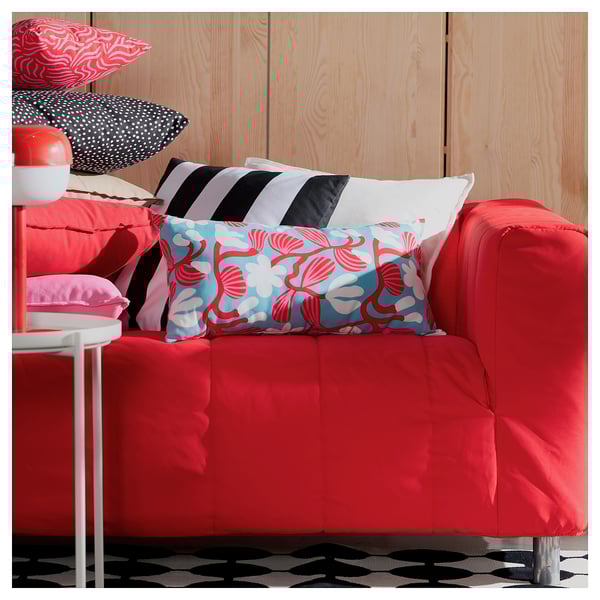 Bright red sofa with multiple colourful pillows, including blue and red floral print. White wood panel wall behind.