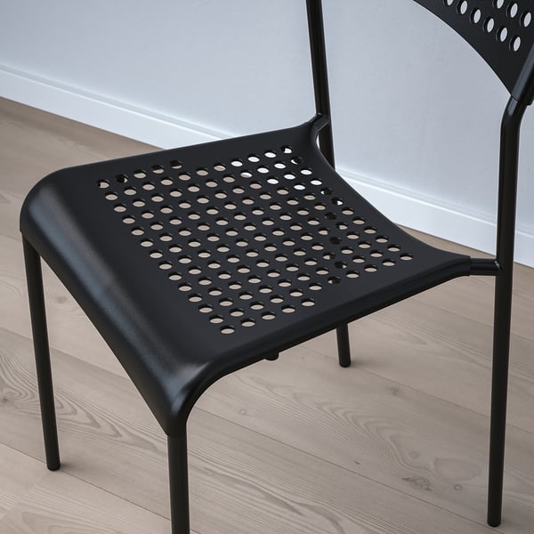 Black modern chair with perforated seat and back for ventilation, placed on light wooden floor.