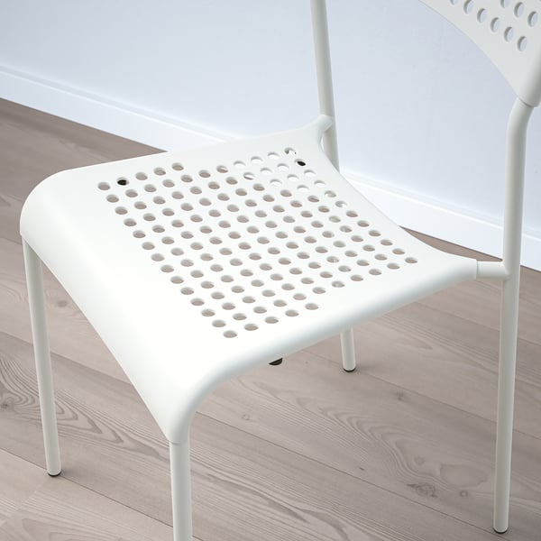 Two modern white chairs with perforated seats, neatly stacked on a light wooden floor, exhibiting sleek design and quality craftsmanship.