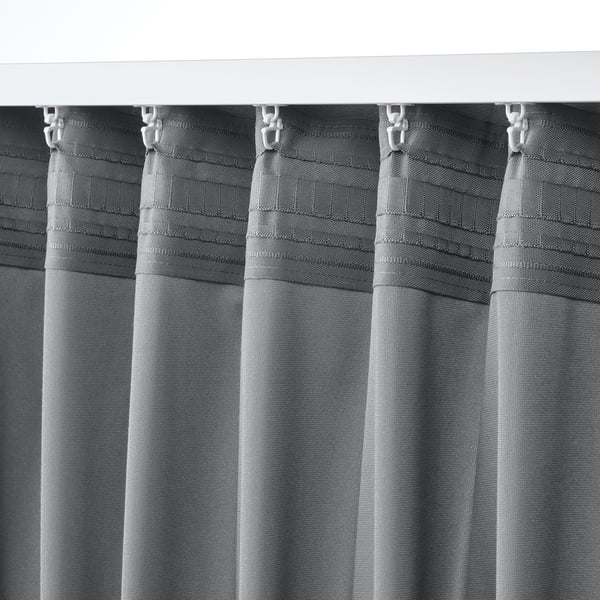 Close-up of SANDSVINGEL curtains. Grey, textured fabric with heading tape and hooks, hanging evenly.