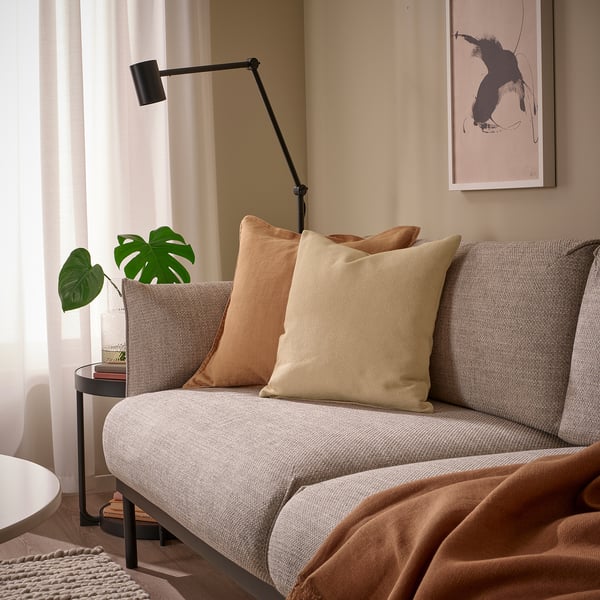 Yellow-beige cushion on grey sofa, recycled cotton & feather-filled, beside plant, calm decor.